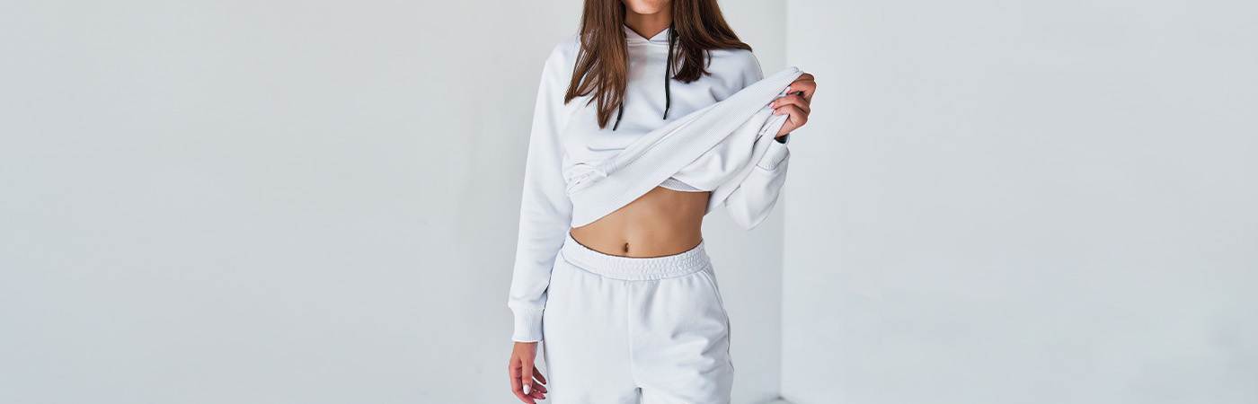 אישה לושבת טרנינג ספורטיבי אופנתי בצבע לבן על רקע קיר בהיר