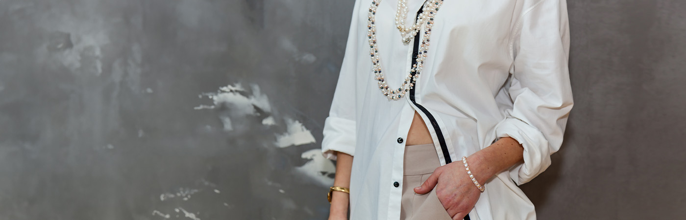 מכופתרת לבנה עם קווי עיצוב אלגנטיים, משולבת עם שרשראות פנינים למראה יוקרתי.