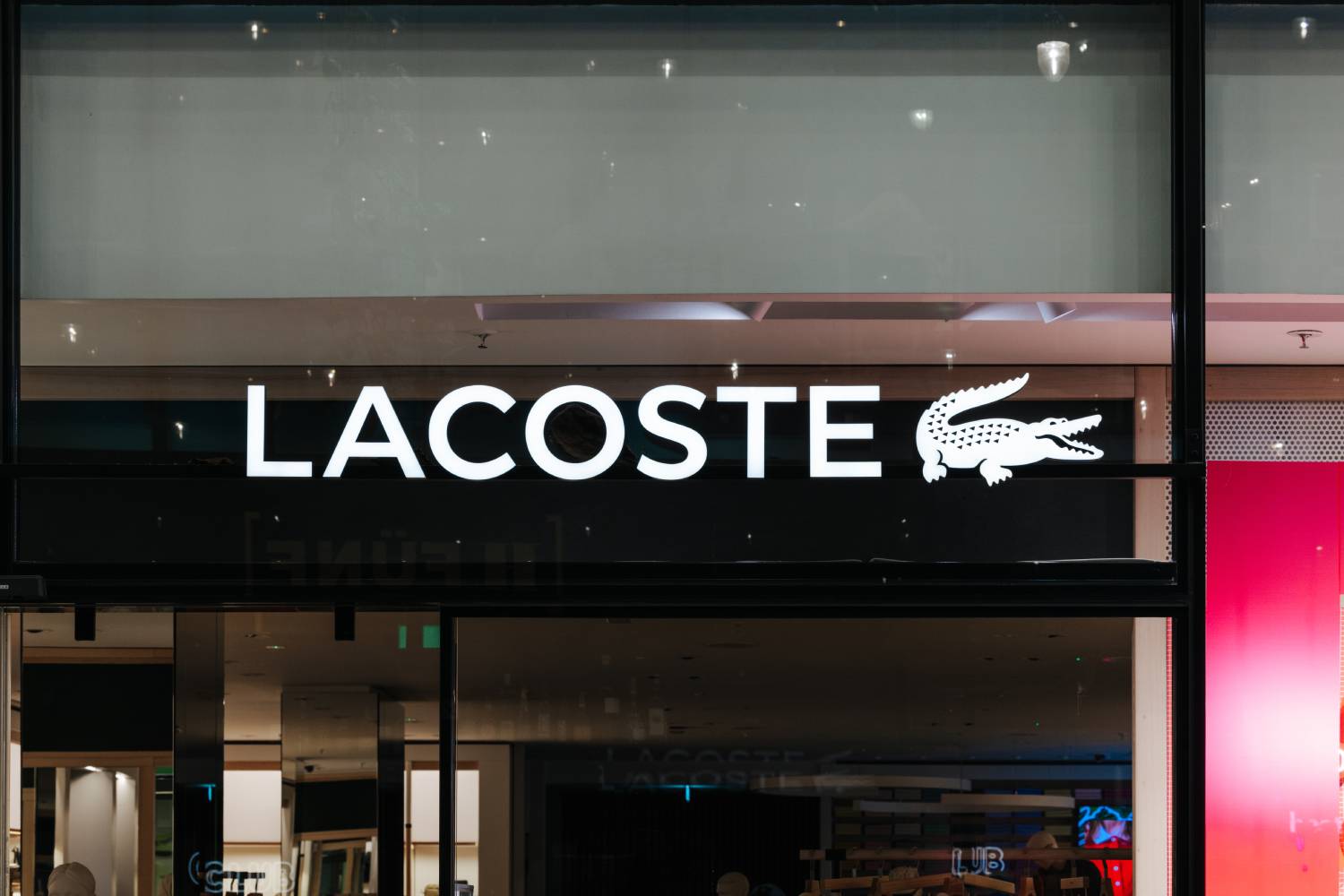 חזית חנות Lacoste עם לוגו המותג המוכר. תקריב של שלט החנות במינכן, גרמניה.